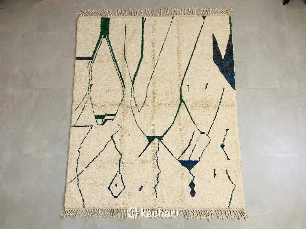 Custom made Beni Ourain Moroccan rug flat lay showing plush cream wool texture with charcoal and sapphire blue geometric diamond patterns and traditional fringe.