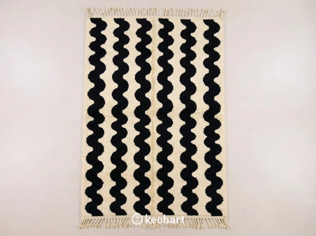 Flat lay view of a custom Beni Ourain Moroccan rug showing the plush cream wool texture, handwoven black geometric diamond pattern, and traditional braided fringe.