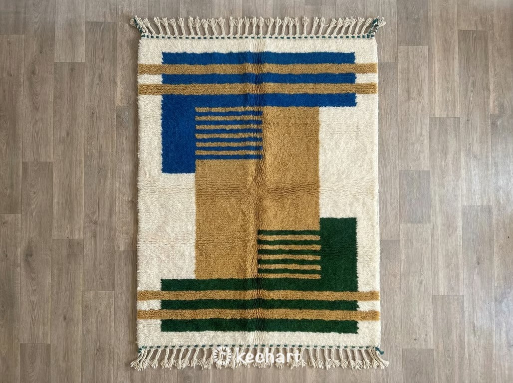 Flat lay view of a custom Beni Ourain Moroccan rug showing plush soft white wool with geometric diamond patterns in Moroccan Blue, Aztec Gold, and Fir Green accents, finished with traditional fringe.