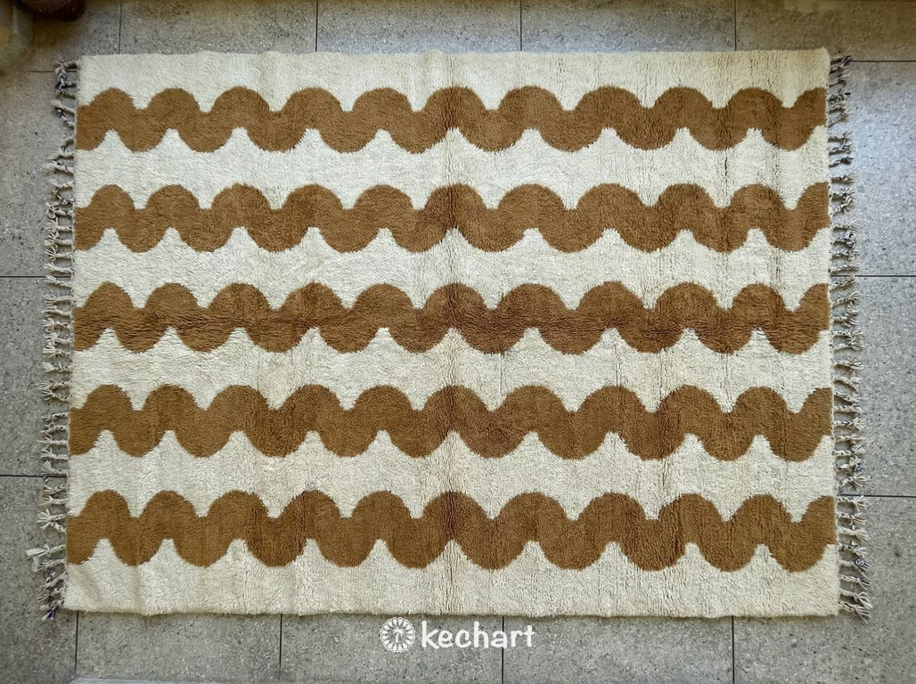 Handwoven custom Beni Ourain Moroccan rug featuring plush cream wool with a subtle camel brown geometric diamond pattern and traditional shag fringe.