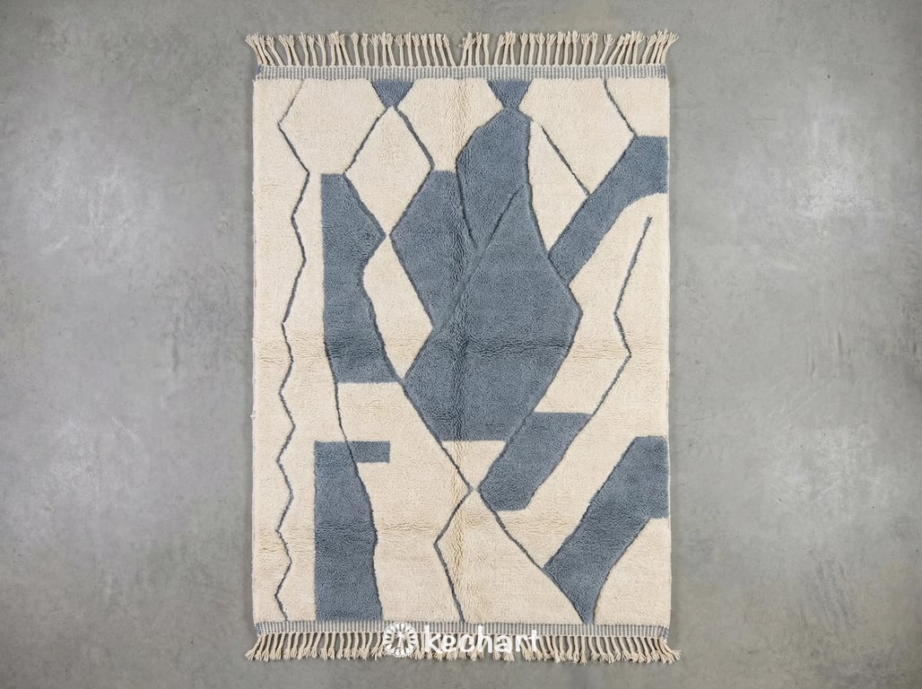 Custom made Beni Ourain Moroccan wool rug with deep shaggy pile, showing natural cream base and dusty blue grey geometric diamond patterns with traditional fringe. Handwoven texture visible.