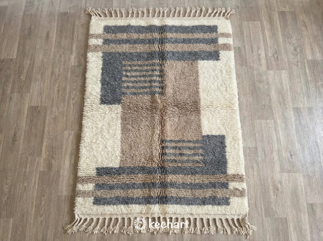 Custom Beni Ourain Moroccan wool rug flat lay, showing plush shaggy texture and geometric diamond pattern in soft grey, taupe, and cream hues with traditional fringe.