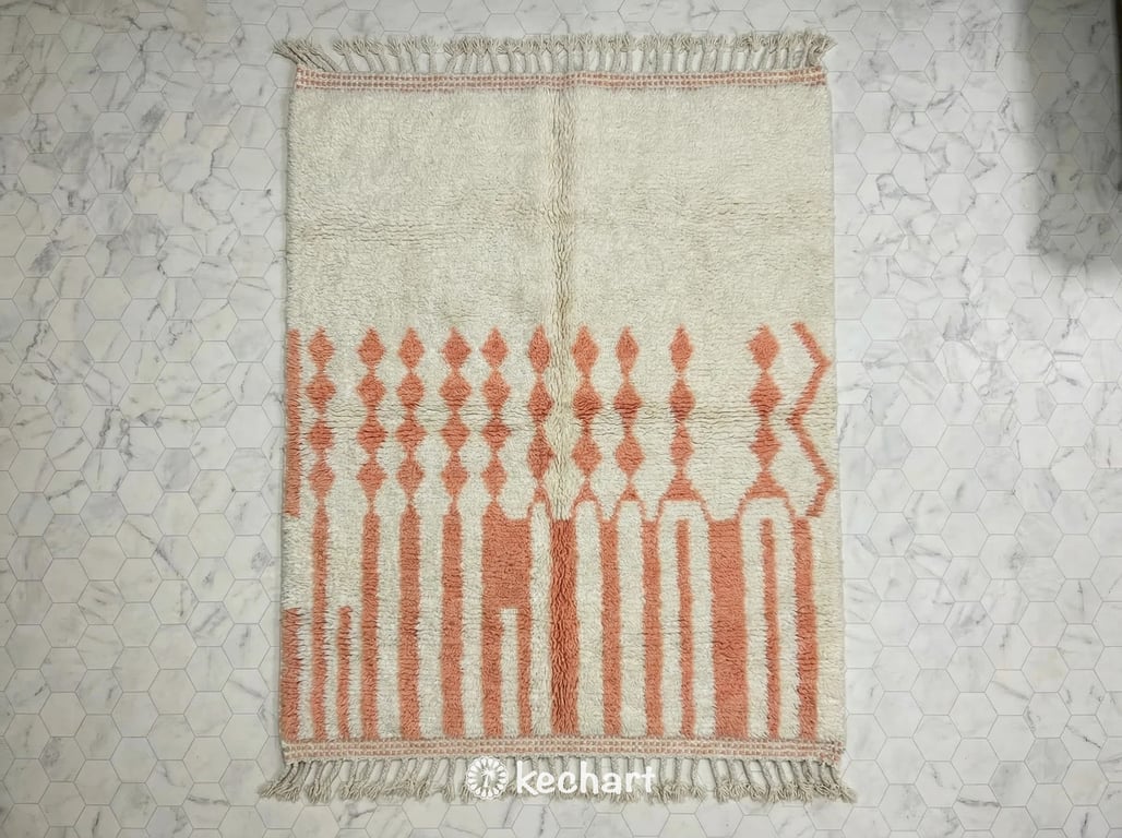 Flat lay view of a custom made-to-order Beni Ourain Moroccan wool rug in light salmon pink with medium density geometric diamond patterns and traditional fringe showing plush texture.