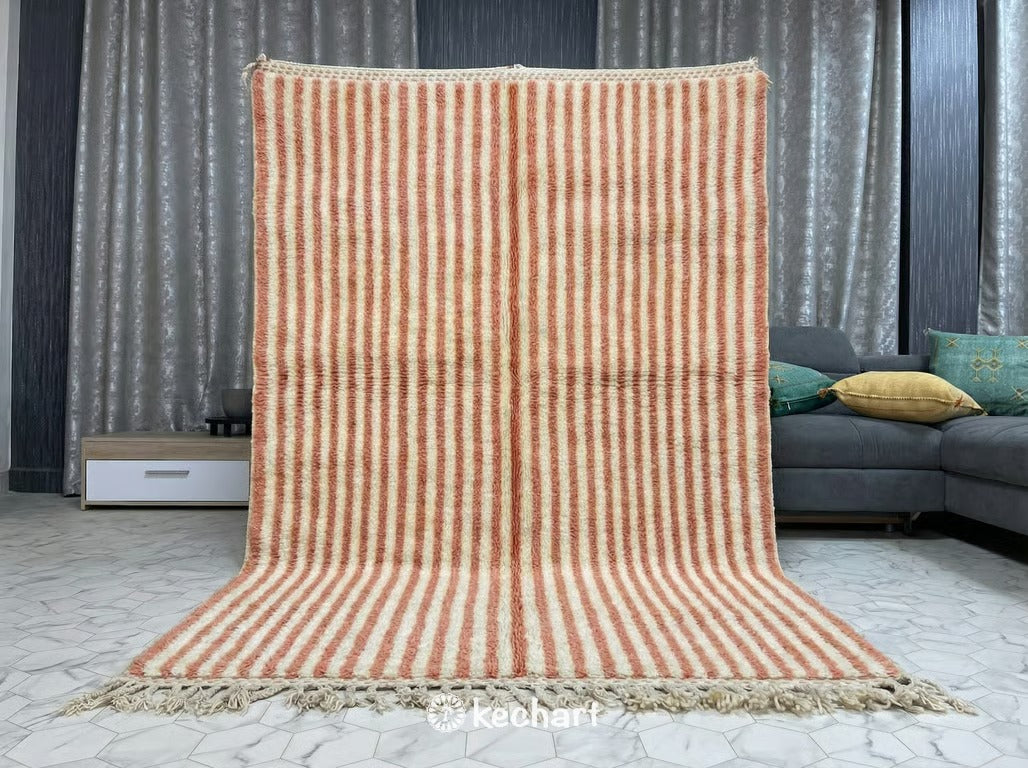 Plush shaggy Moroccan wool rug in a bohemian bedroom setting, partially under a queen-sized bed with soft textures, highlighting the warm salmon diamond motifs against the cream base.